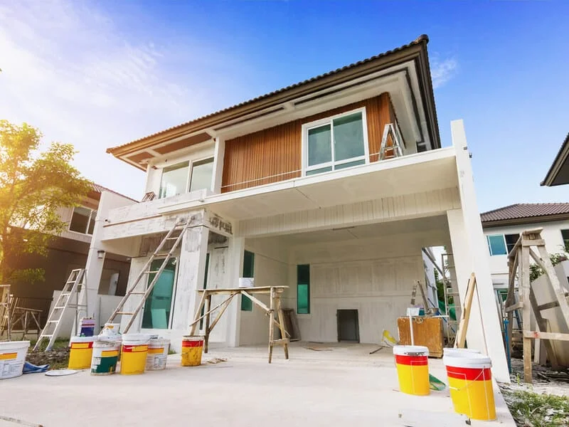 Reforma residencial em fachada de casa Casa de dois pavimentos durante reforma de fachada com escadas, ferramentas e materiais de pintura