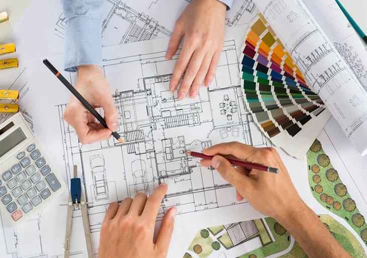 Profissionais analisando planta arquitetônica com desenhos técnicos, amostras de cores e materiais de projeto