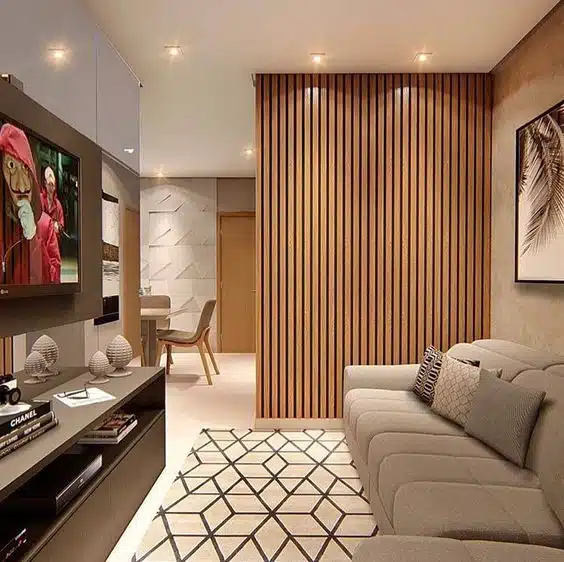 Divisão parcial entre sala de TV e ambiente adjacente Sala de TV com painel ripado de madeira separando parcialmente outro ambiente ao fundo
