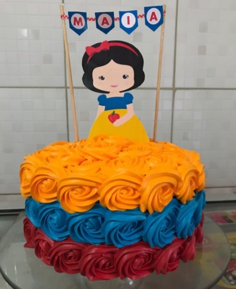 11 Ideias de Bolo de Branca de Neve para Festas Inesquecíveis 10 Bolo infantilizado com rosas de chantininho, placa de papel da princesa baby e faixa personalizada.