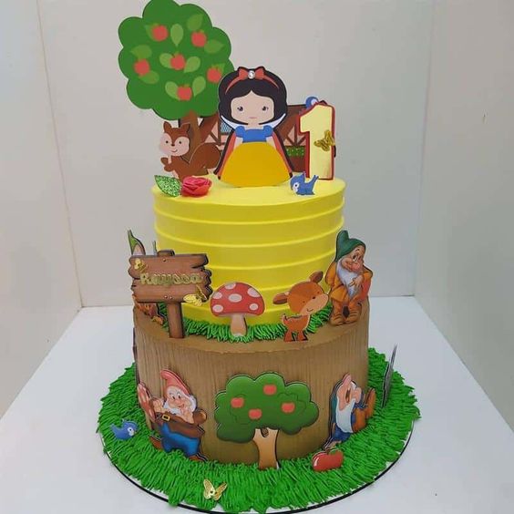 11 Ideias de Bolo de Branca de Neve para Festas Inesquecíveis 7 Bolo de dois andares com amarelo em destaque, elemento de tronco de árvore e floresta encantada.