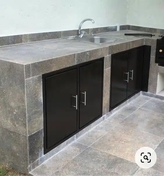 Bancada de cozinha revestida em peças cinza com portas pretas sob a pia