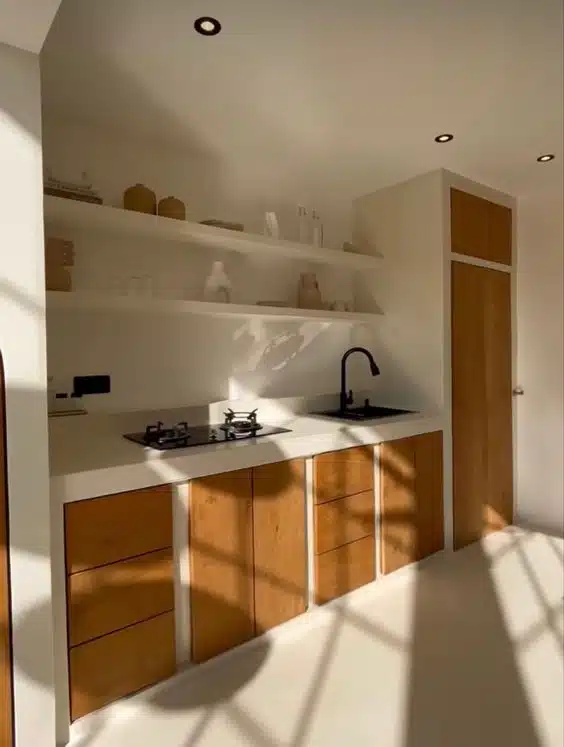 Cozinha clara com nichos abertos, portas de madeira e luz solar entrando pela janela