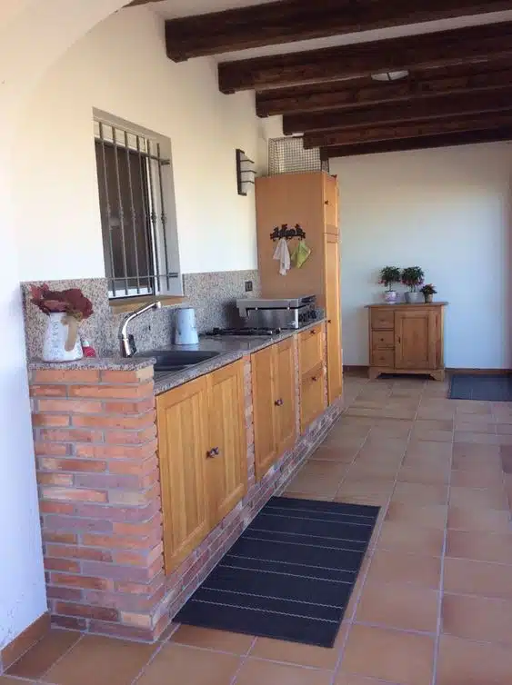 Cozinha rústica com base de tijolos aparentes, portas de madeira e vigas no teto