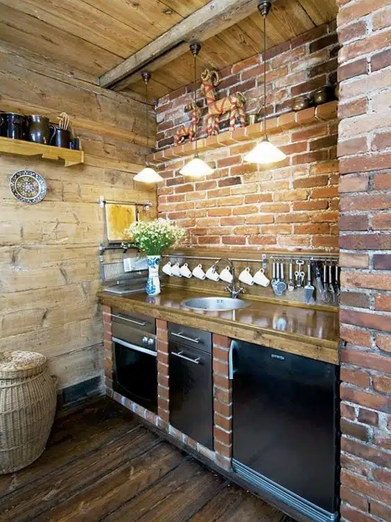 Cozinha rústica compacta com tijolos aparentes, madeira, pia e eletrodomésticos embutidos