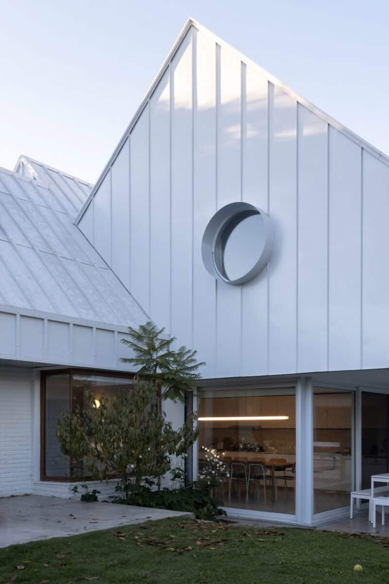 Detalhe do terceiro gable, envolto em metal branco, com uma janela circular para uma estética moderna.
