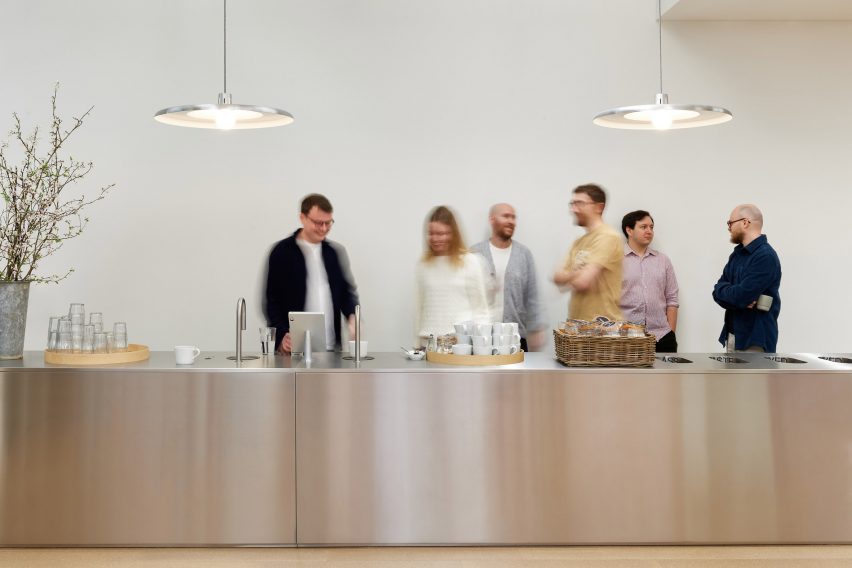Um close do balcão de aço inoxidável, onde os funcionários se encontram para café e interação, enfatizando a atmosfera colaborativa do espaço.