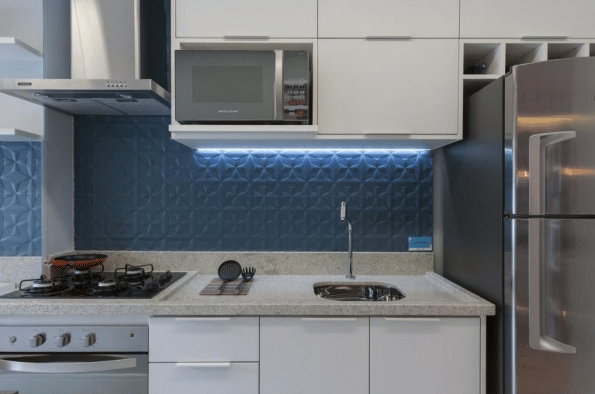 Como Escolher a Cerâmica Ideal para a Cozinha: Beleza, Praticidade e Resistência 6 Cerâmica para cozinha: revestimento azul na parede, móveis planejados em marcenaria branca, bancada de granito com cooktop preto e coifa de inox – Projeto: Adriana Fontana