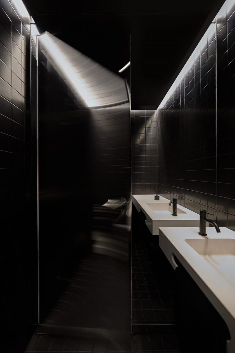 Espaço Colaborativo Inovador para o Trabalho Pós-Covid. 4 Banheiro com revestimento em azulejos pretos contrastando com o interior predominantemente branco do espaço.
