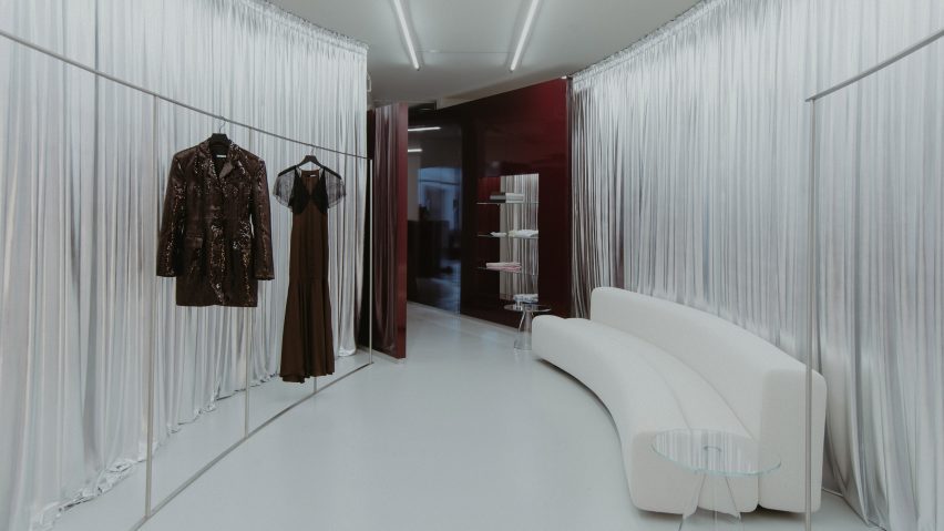 Incrível loja Rotate em Copenhague com design inovador. 4 Cortinas prateadas que cercam uma sala oval, com um sofá branco curvilíneo.