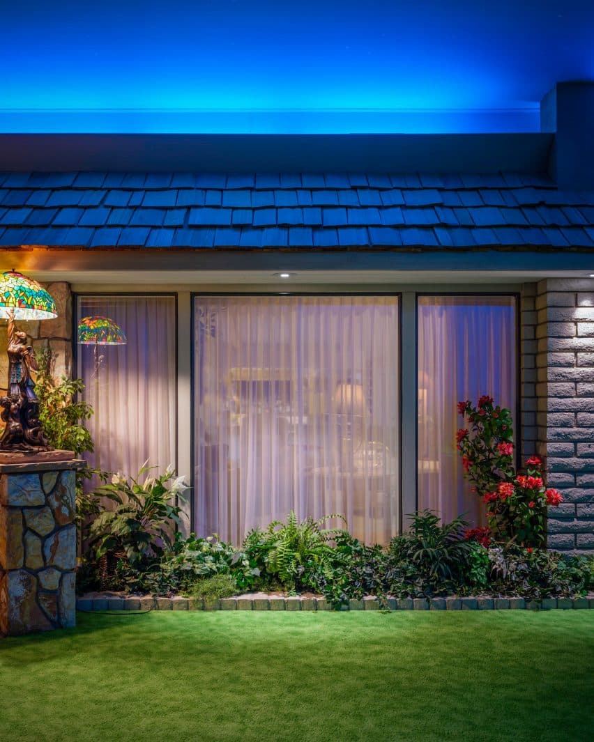 Bunker apocalíptico exibe kitsch extravagante e peculiaridade impressionante. 2 Um espaço verde artificial dentro da casa com uma janela, cercado por árvores artificiais e cenários pintados, representando uma vista externa.