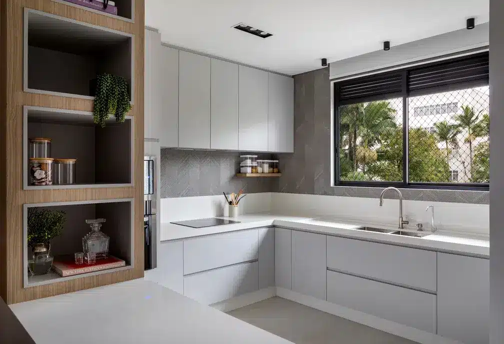 Cozinha branca com meia parede cinza, janela e luz natural. O projeto confere um espaço agradável para curtir um momento importante no local (Projeto: Bruna Balestieri Arquitetura e Interiores)