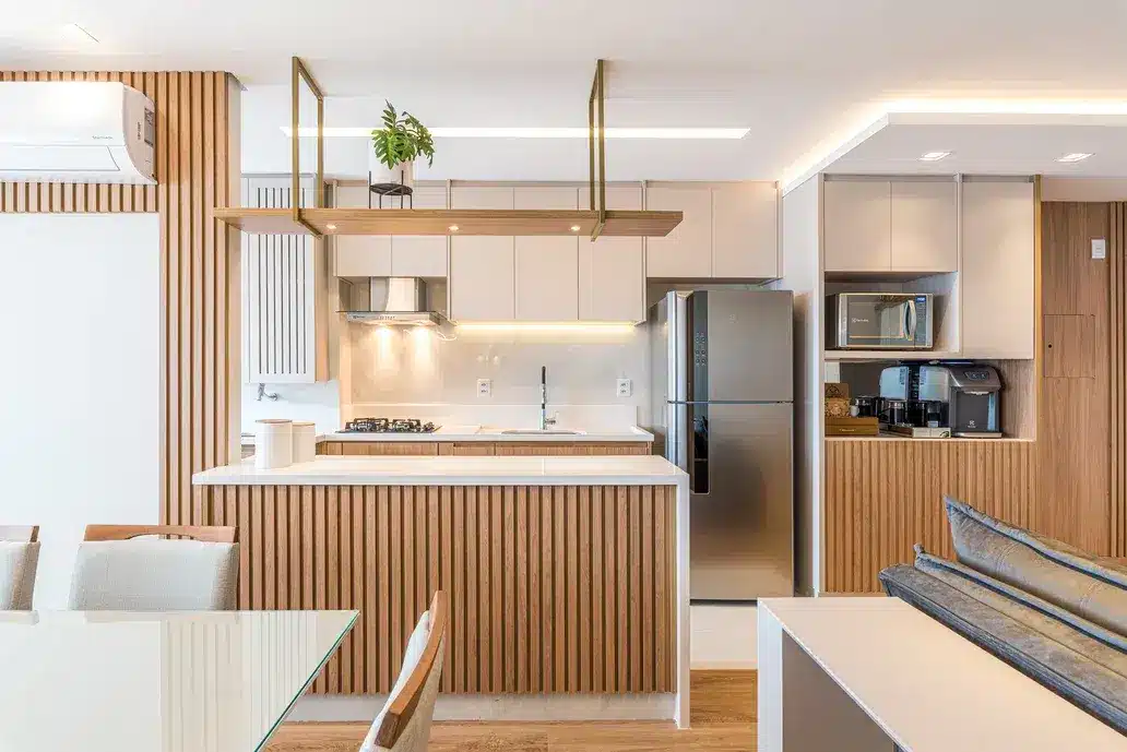 Cozinha com revestimento amadeirado e cores neutras, com eletrodomésticos de cozinha visíveis. Os eletrodomésticos criam um ambiente mais moderno, além de funcional (Projeto: Cinthia Claro Arquitetura)