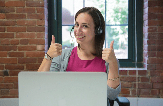 Imagem de uma modelo fotográfica fazendo sinal de positivo em frente a um notebook gigante.