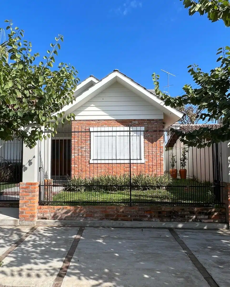 Fachada simples de casa térrea com tijolo e telhado Casa térrea simples com tijolos aparentes, telhado inclinado, jardim frontal e grade metálica