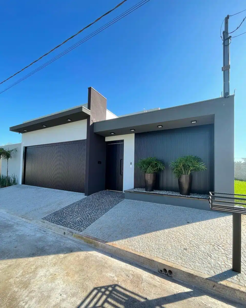 Fachada de casa simples com garagem Fachada residencial em preto e branco com garagem ampla, acesso de pedestres e vasos com plantas