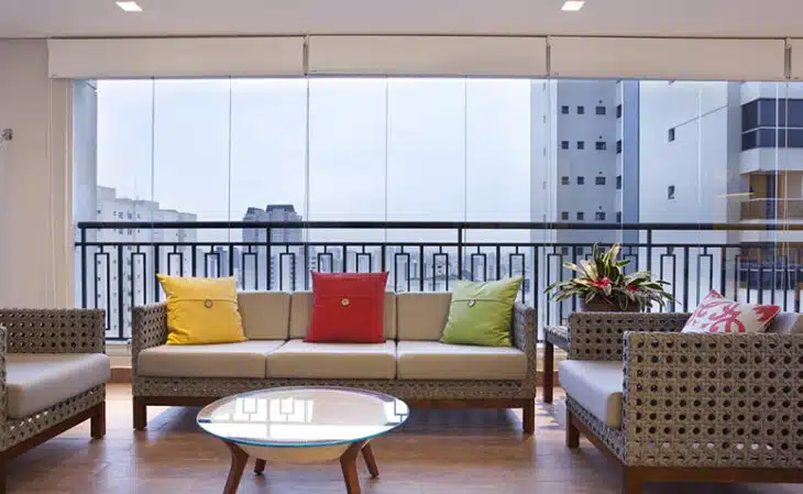 Cortina de vidro em sala integrada à varanda Varanda de apartamento fechada por painéis transparentes com sofá e poltronas
