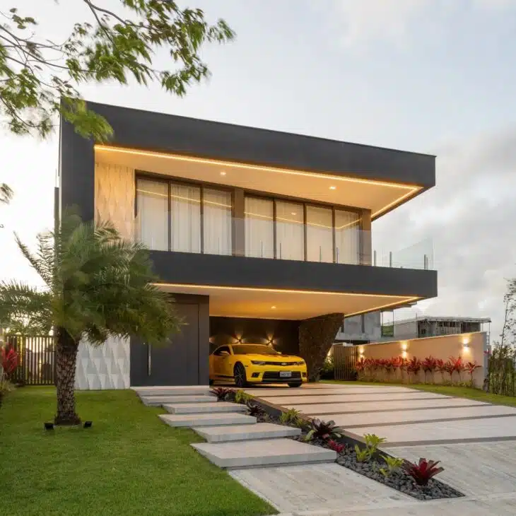 Garagem integrada à fachada de sobrado moderno Sobrado contemporâneo com garagem integrada, jardim e volumes escuros