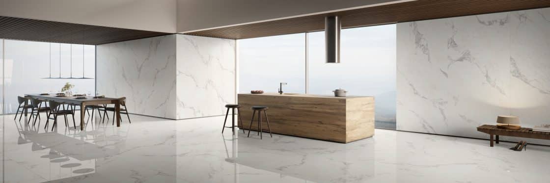 Revestimento de mármore: opções para um projeto mais sofisticado 10. 10 Cozinha com revestimento que reproduz mármore no piso e nas paredes; ilha em madeira com cooktop e banquetas, e uma mesa de jantar.