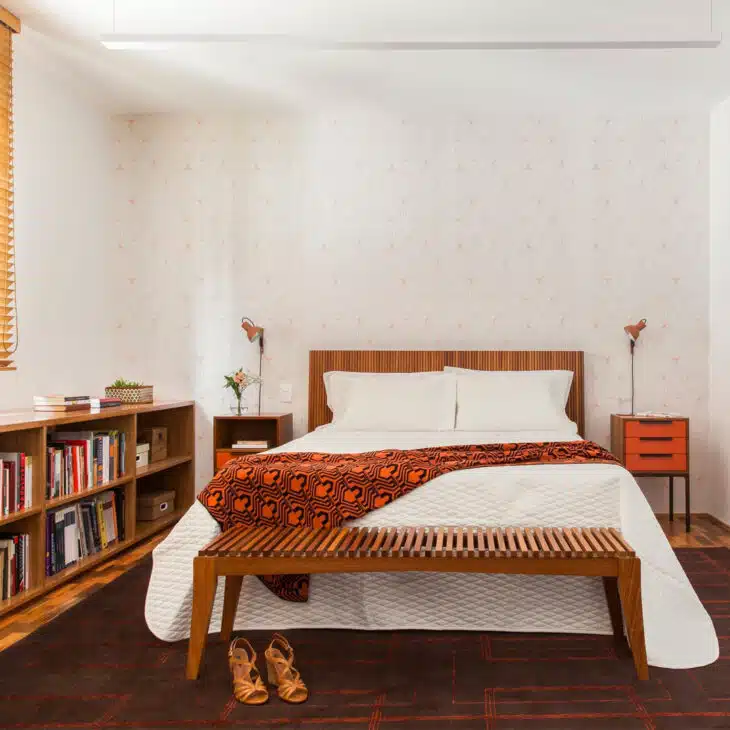 Quarto com cama de madeira, estante baixa, banco e manta estampada em tons quentes