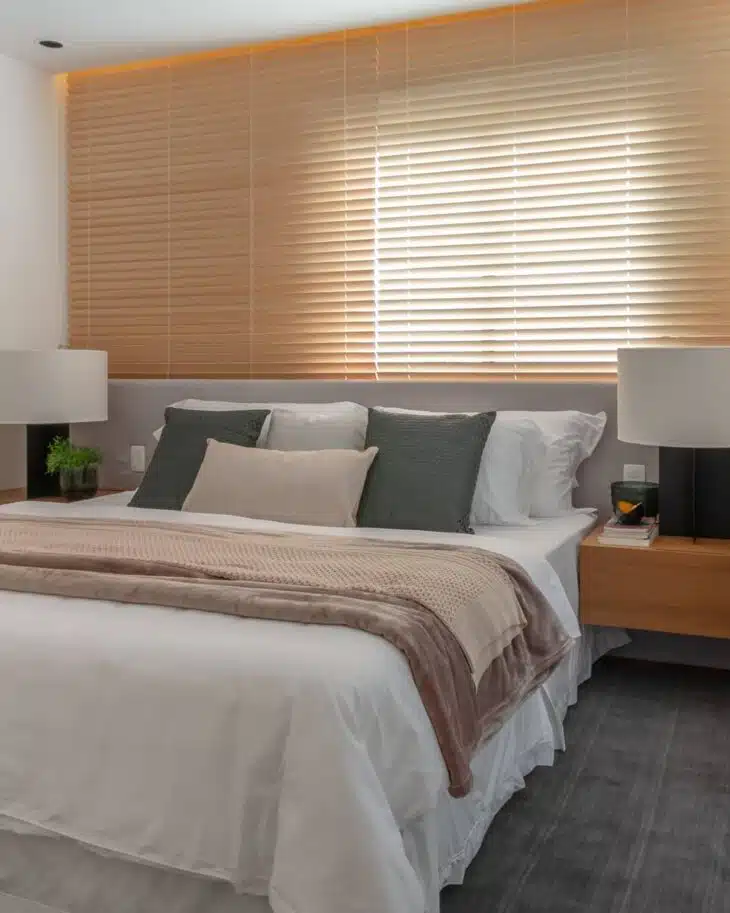 Quarto de casal com persiana de madeira, roupa de cama neutra e mesas laterais