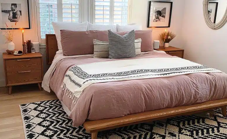 Quarto decorado com roupa de cama rosa, madeira, tapete estampado e tons neutros