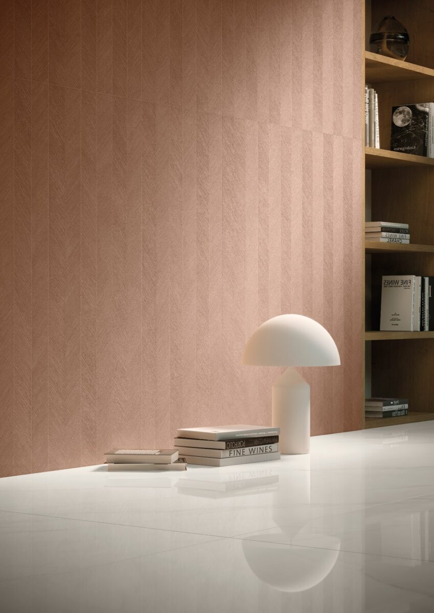 Porcelanato Carrara: A beleza do mármore com as vantagens do revestimento 10. 7 Detalhe de ambiente com piso em mármore carrara. Há uma luminária e livros, tudo na frente de uma parede rosada.