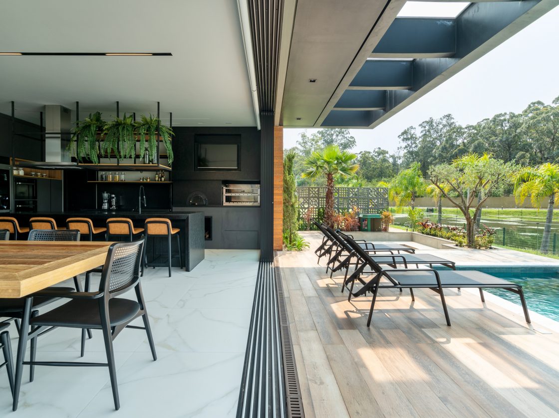 Transforme sua Área Externa: Revelamos as Melhores Opções para Dar Vida ao Seu Espaço! 9 Varanda integrada com espaço gourmet, porcelanato amadeirado e porcelanato marmorizado se encontram, vegetação abundante, piscina e área gourmet em madeira e preto