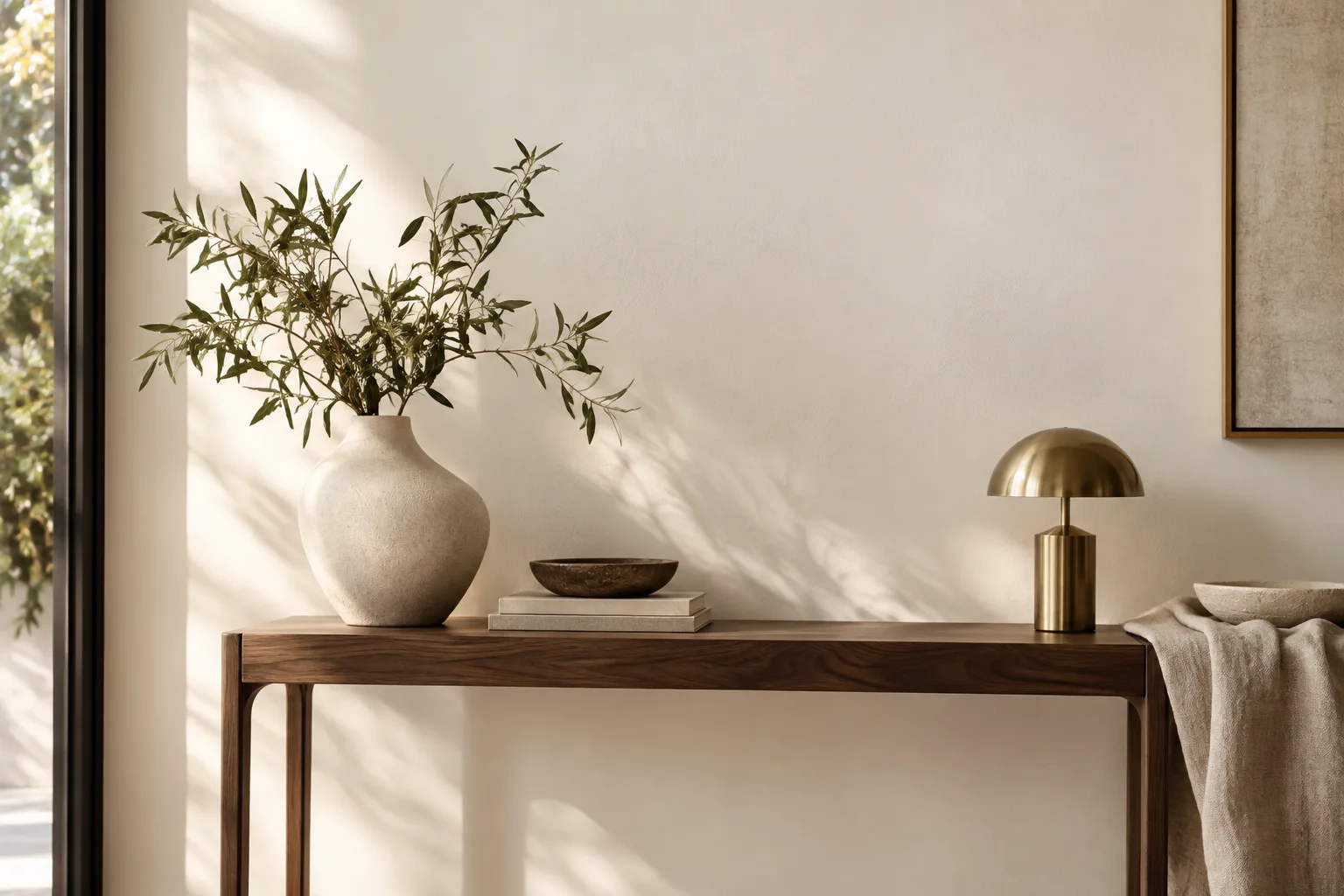 Branco quente na decoração: tons, combinações e como escolher 7 Detalhe de parede branco marfim com aparador de madeira escura, vaso de cerâmica e luminária de metal.